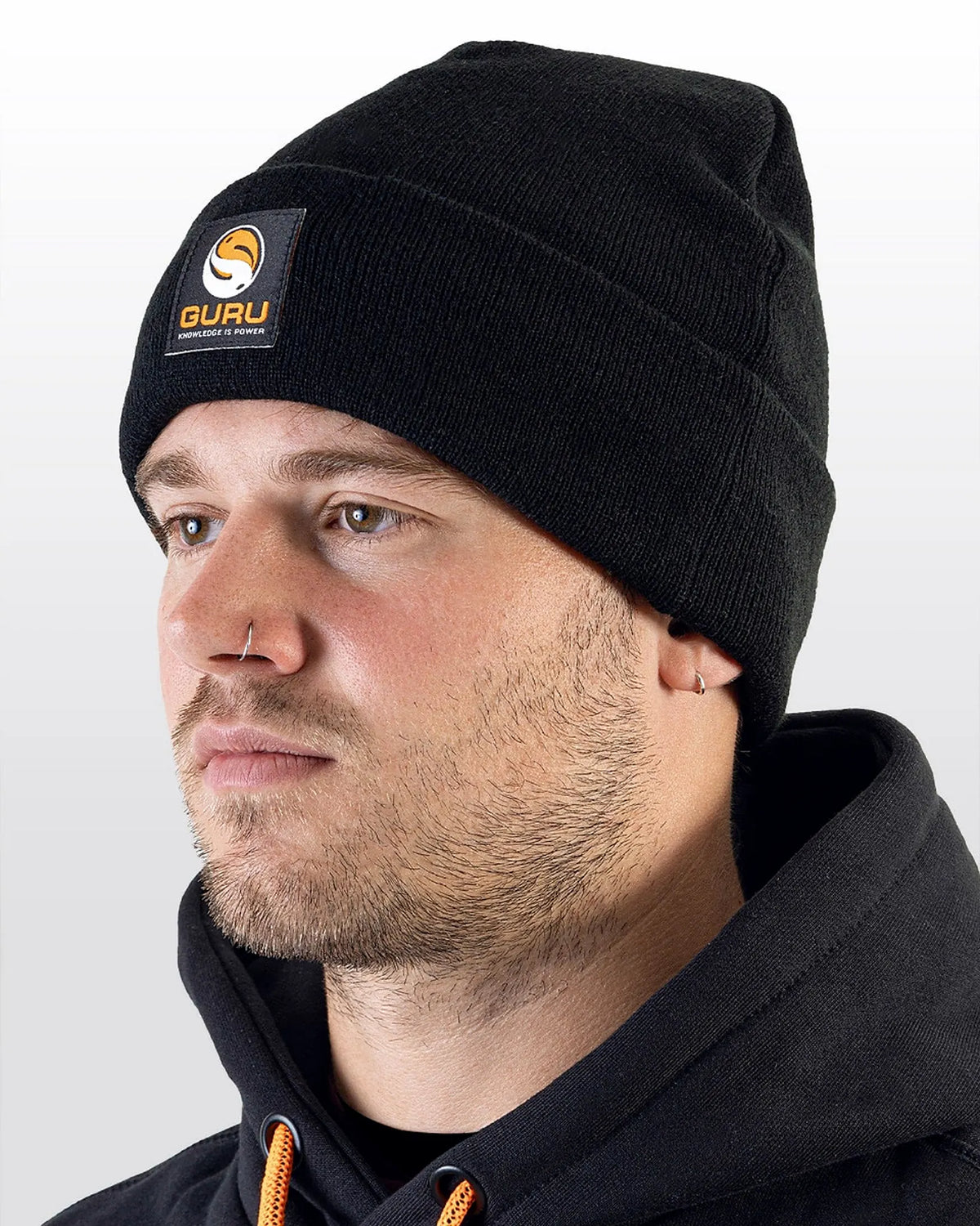 Guru Black Patch Beanie – gedragen in een studioportret met de zwarte omslag en oranje Guru-patch zichtbaar