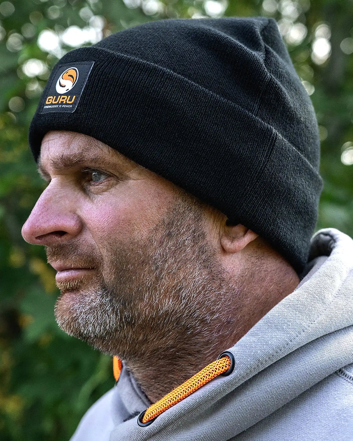 Guru Black Patch Beanie – gedragen in zijprofiel met de zwarte omslag en Guru-patch duidelijk zichtbaar