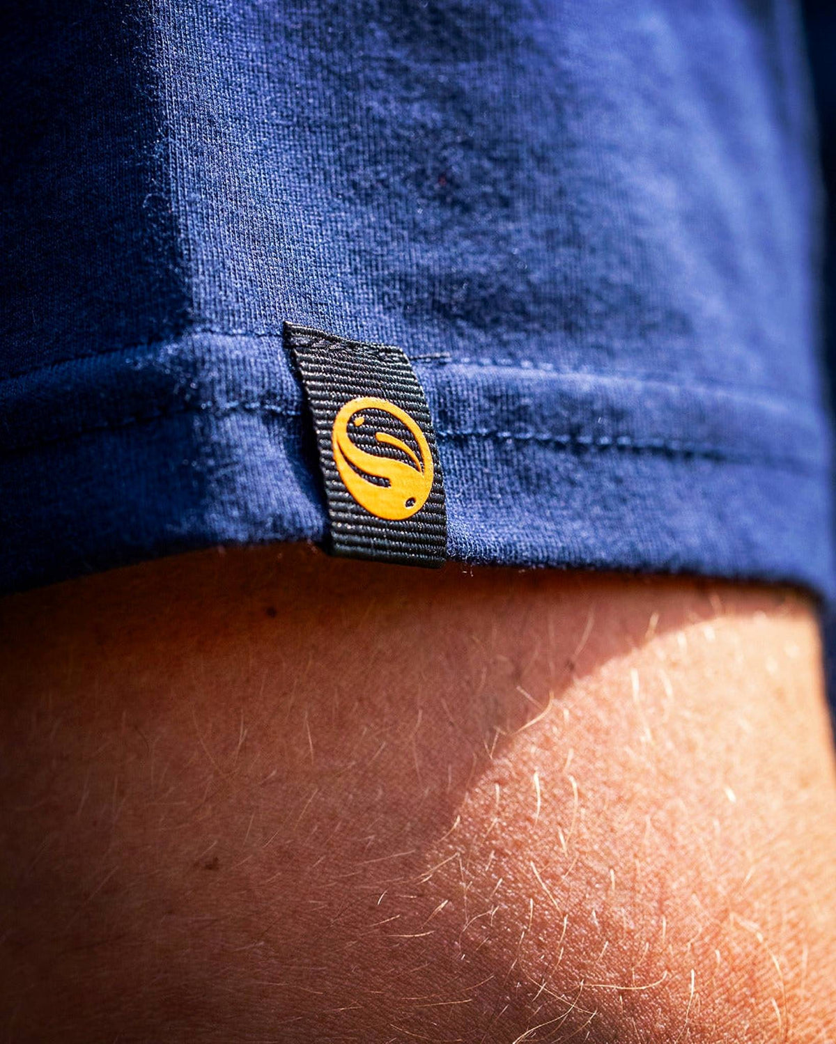 Guru Glitch Navy Tee – close-up van het geweven Guru-mouwlabel, de zoom en de marineblauwe stof