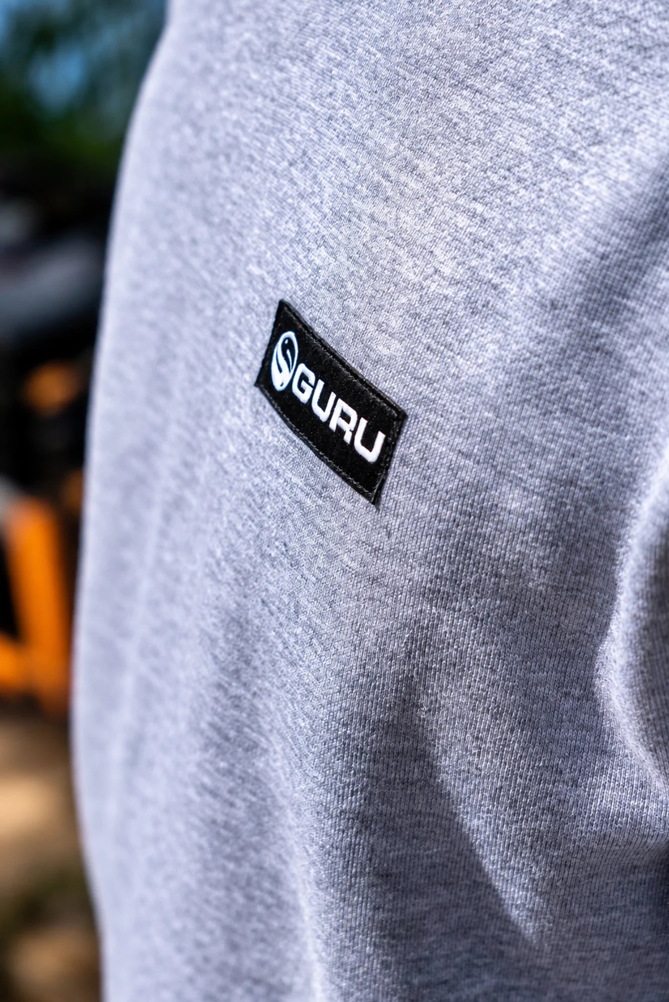 Close-up van de zwarte Guru-borstpatch op de grijze gemêleerde sweaterstof