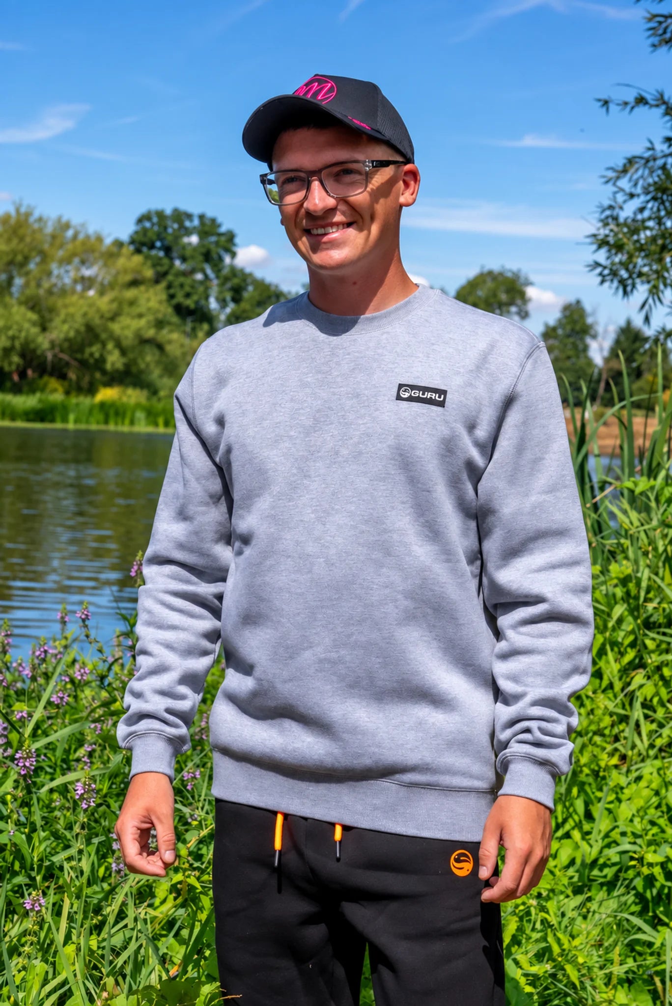 Guru Patch Crewneck Grey gedragen aan de waterkant, met zicht op de pasvorm en ribboorden