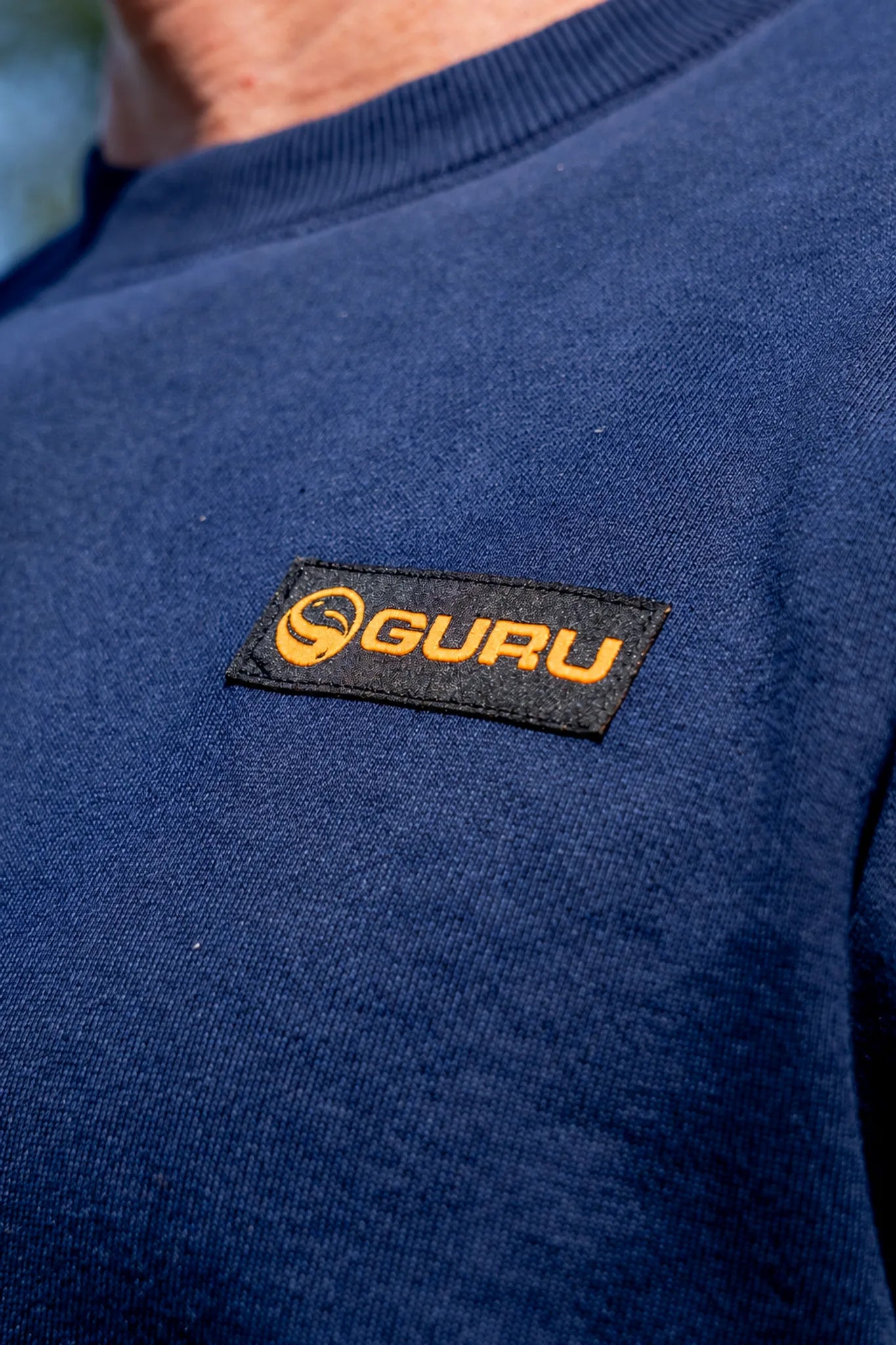 Oranje Guru-logo op de zwarte borstpatch van de marineblauwe Patch Crewneck