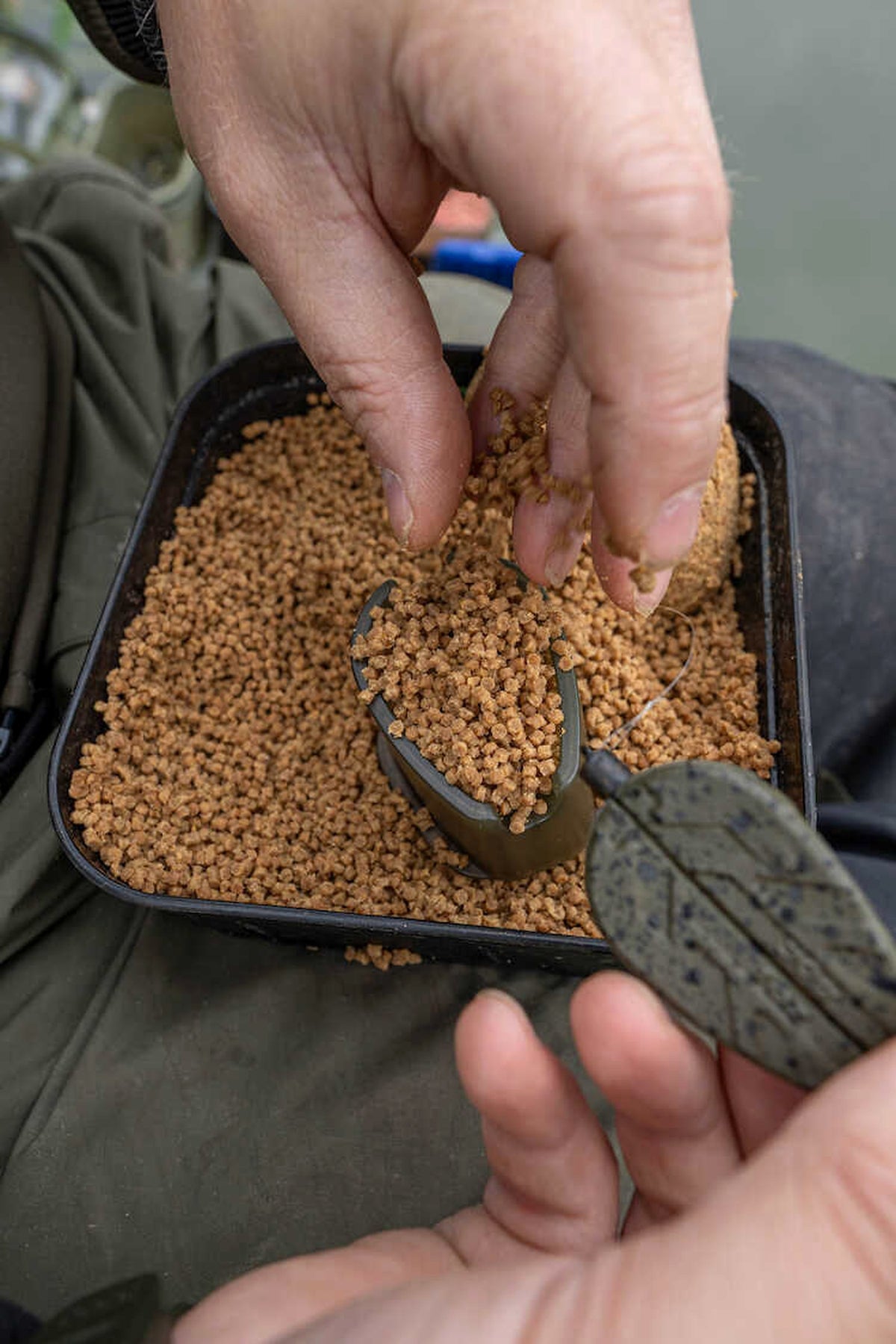 Korum Camo Method Feeder vullen met pellets in de methodmal boven een aasbak