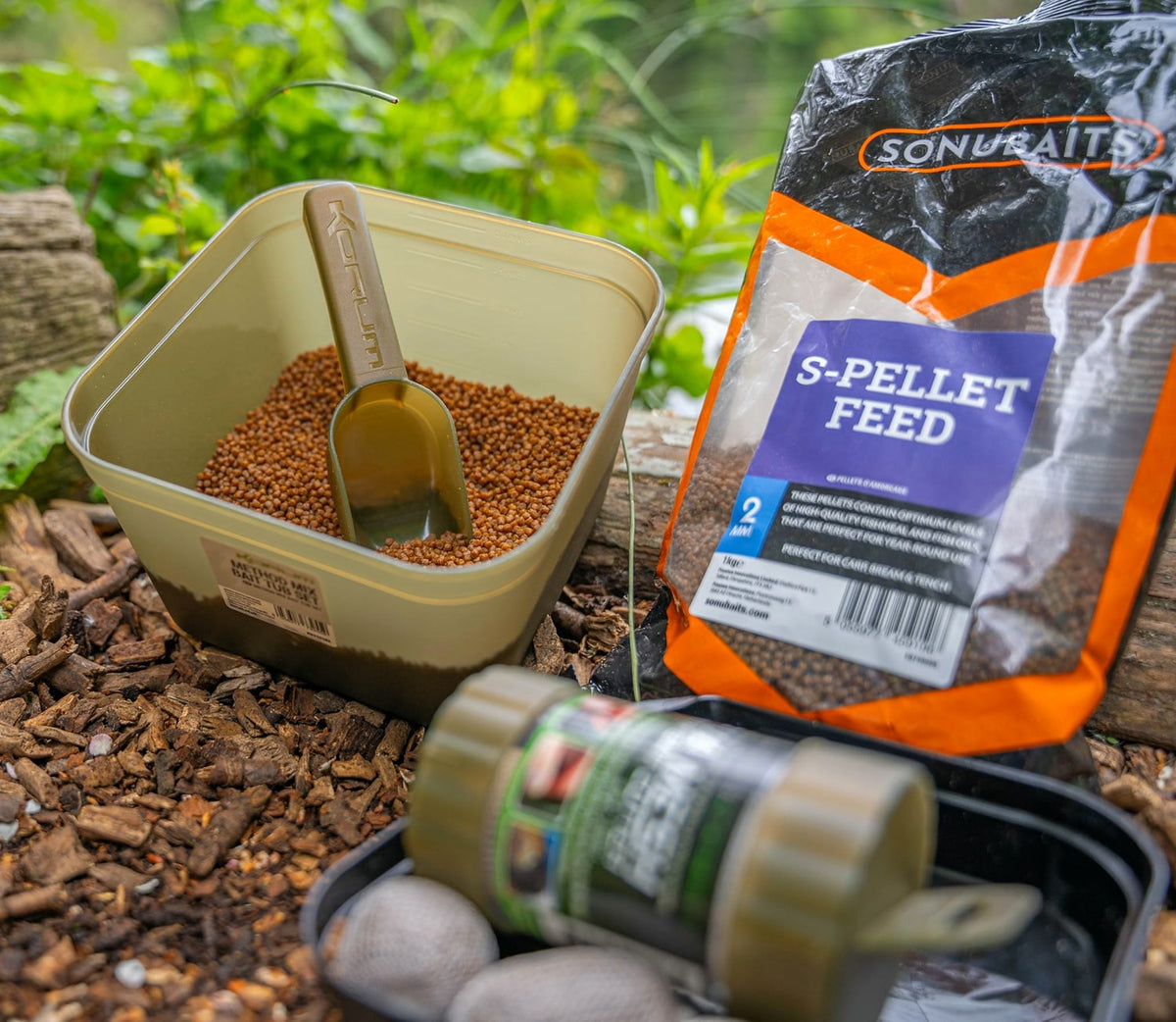 Korum Method Mix aasbak met pellets en voerschep naast een zak S-Pellet Feed en aasaccessoires