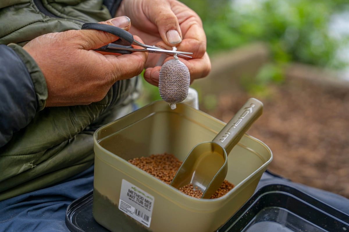 Gevuld PVA-zakje afknippen boven de Korum Method Mix aasbak met pellets en voerschep