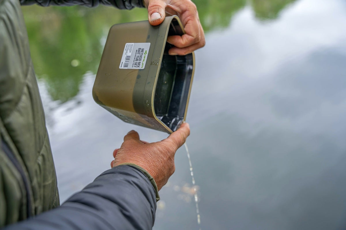 Water uit de schuin gehouden Korum Method Mix aasbak afgieten terwijl de zwarte binnentray wordt vastgehouden