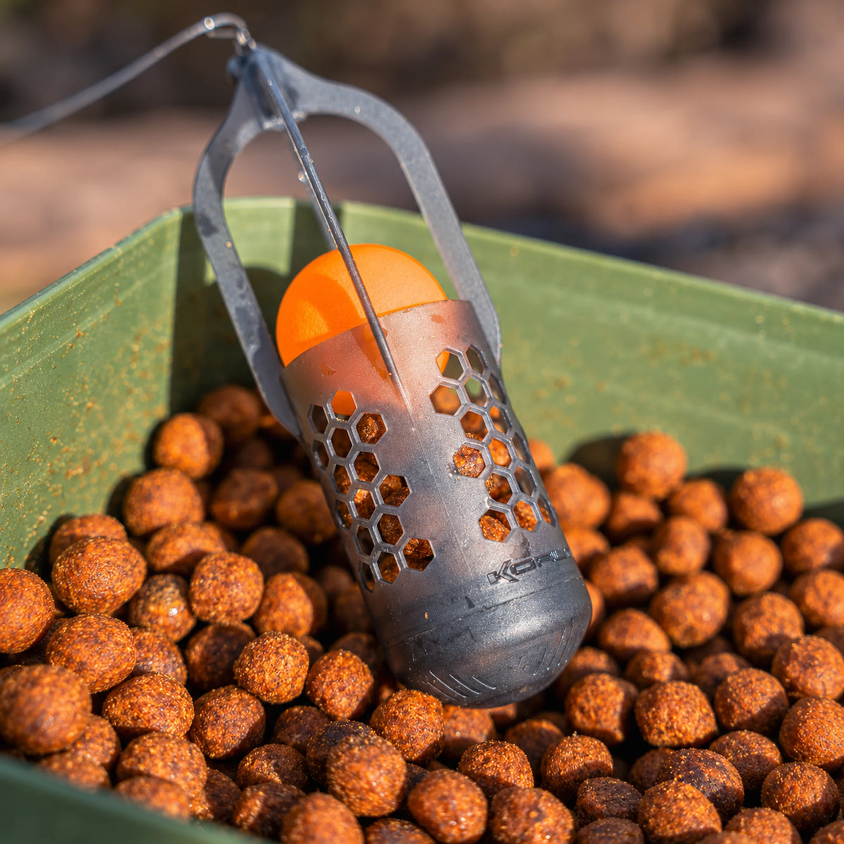 Korum Surface Feeder Float K0320112 – rechtopstaande voerkorf met oranje EVA-bal en pellets in een aasbak
