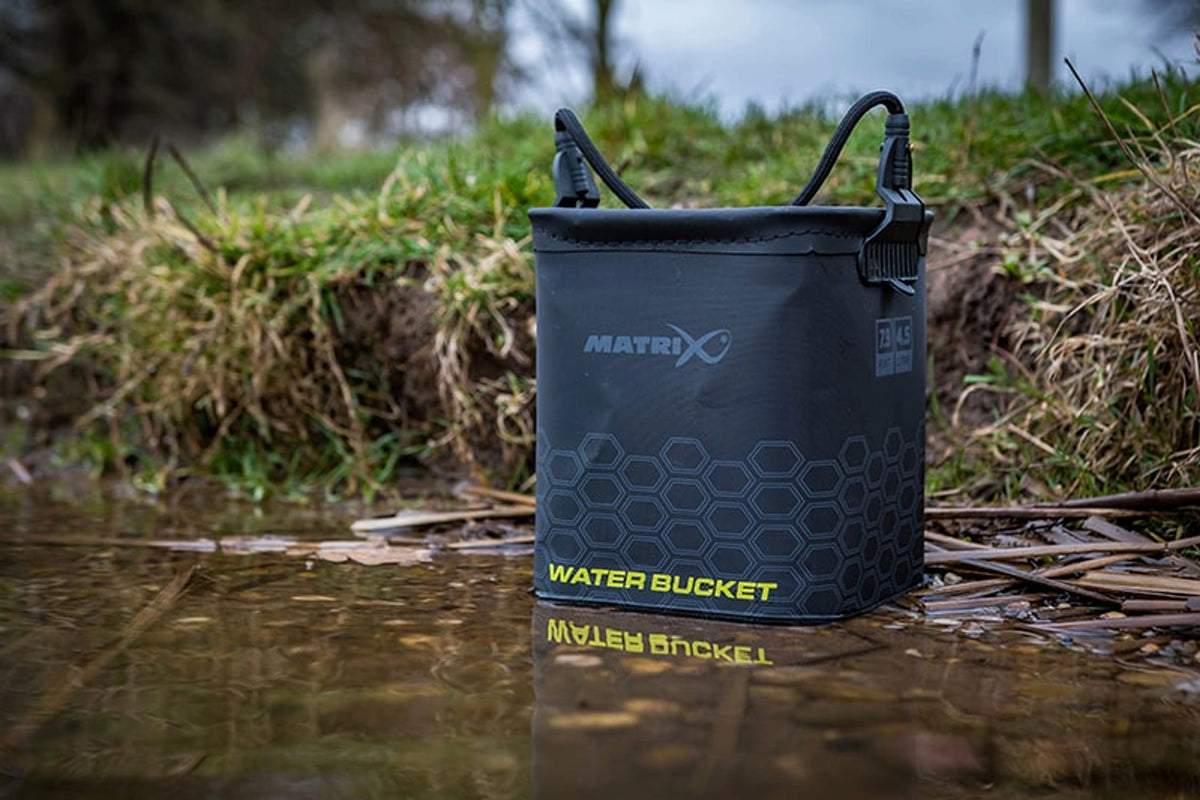 Matrix EVA Water Bucket rechtop in ondiep water bij een begroeide oever