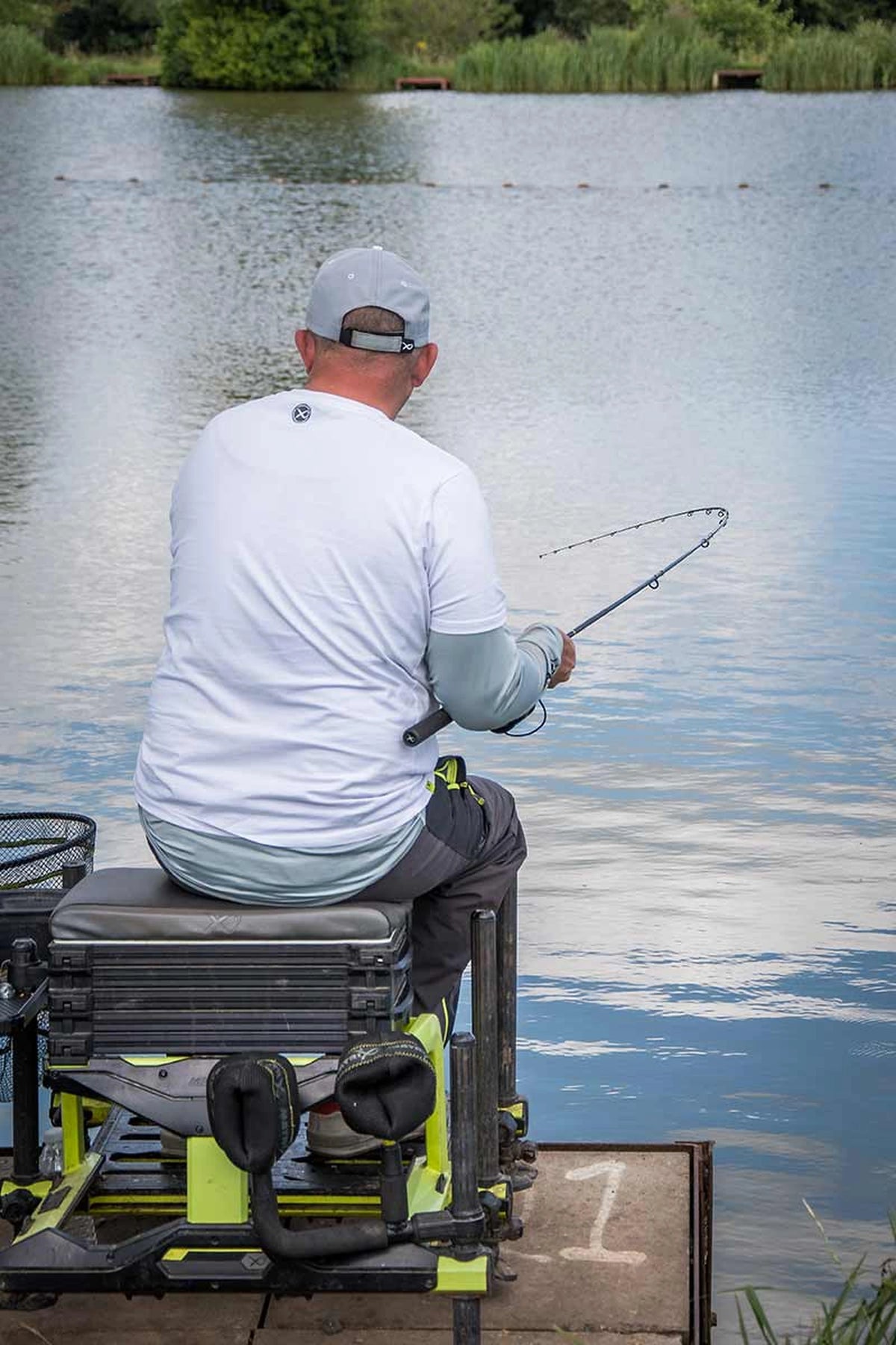 Matrix Aquos Ultra-C Feeder Rod – achteraanzicht van een zittende visser die een vis drilt met de gebogen hengel
