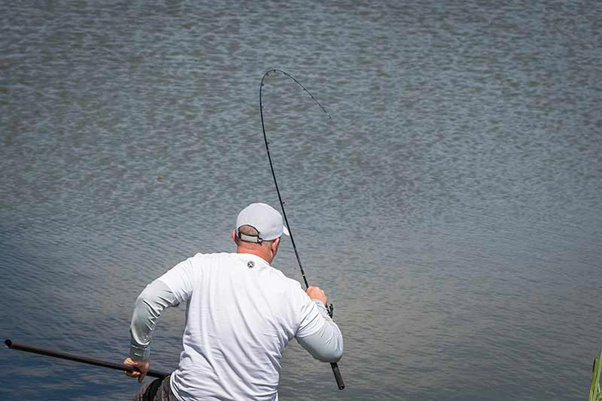 Matrix Aquos Ultra-C Feeder Rod – visser met sterk gebogen hengel tijdens het drillen en een schepnetsteel in de andere hand