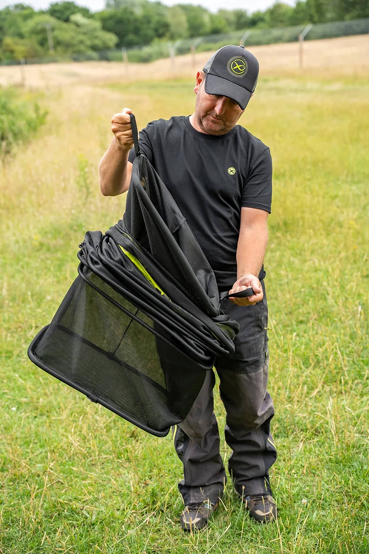 Visser toont de twee handgrepen van een ingevouwen Matrix Carp Safe Keepnet aan de waterkant