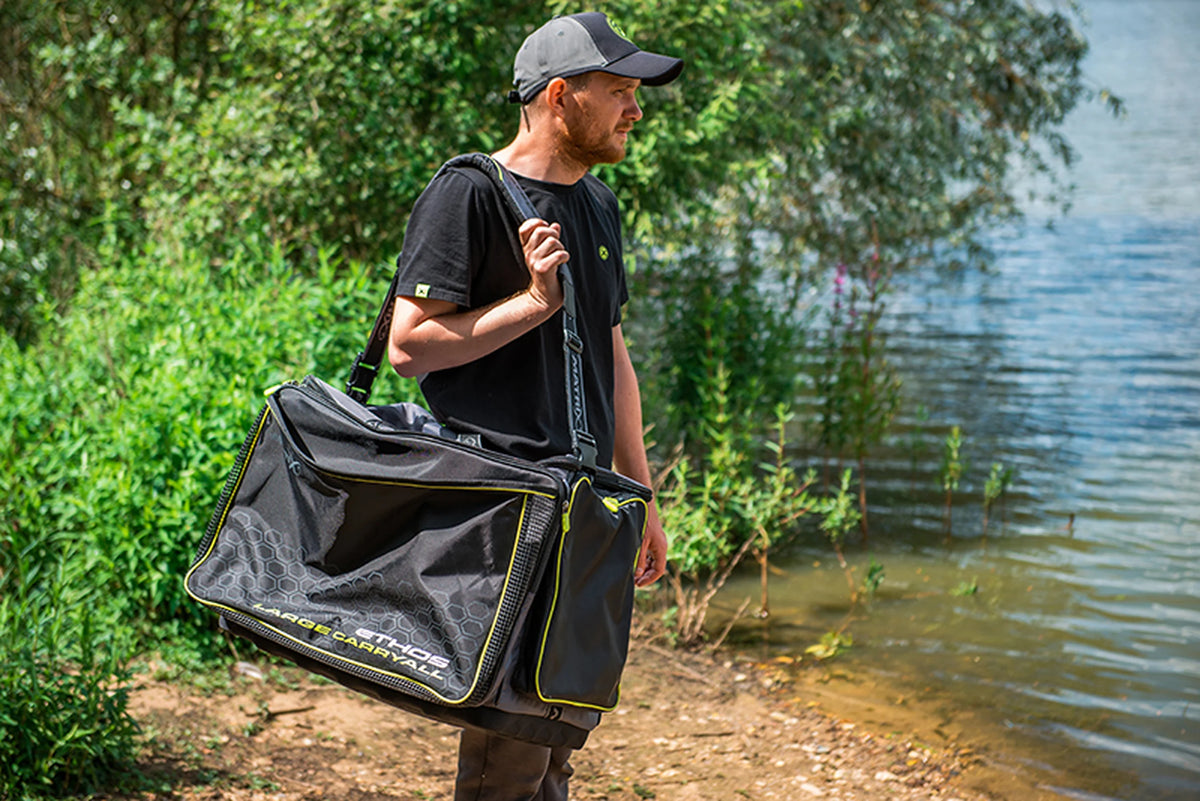 Matrix Ethos Large Carryall – visser draagt de grijze en zwarte tas over zijn schouder aan de waterkant