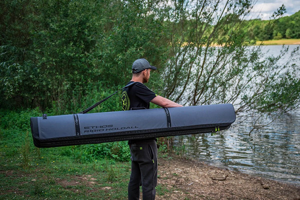Matrix Ethos Rigid Holdall – visser draagt het lange grijze foedraal aan de schouderriem langs het water