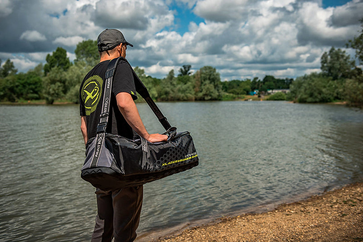 Matrix Ethos XL Accessories Bag – visser draagt de accessoiretas over de schouder aan het meer