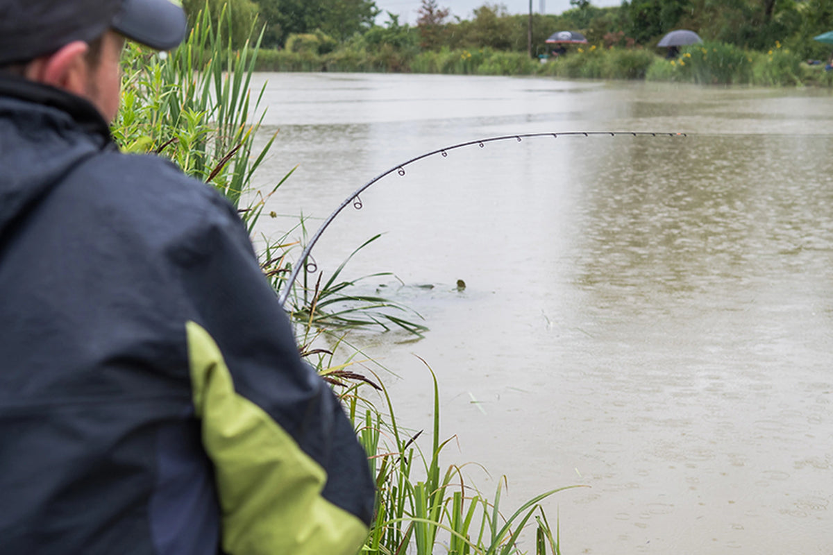 Matrix Ethos XR-C Bomb Rod 9ft – gebogen hengel boven het water tijdens het vissen, gezien achter de schouder van de visser