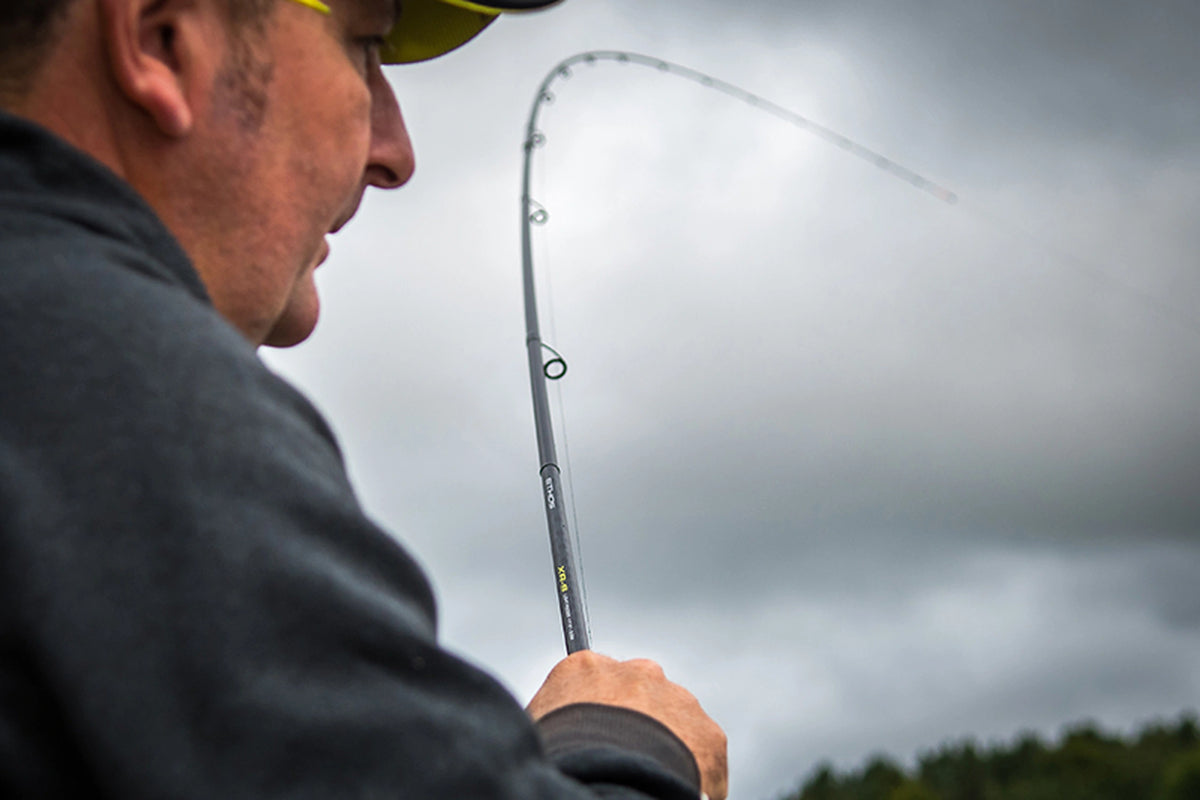 Matrix Ethos XR-S Feeder Rod in gebruik – close-up naast de schouder van een visser met de gebogen blank tegen een bewolkte lucht
