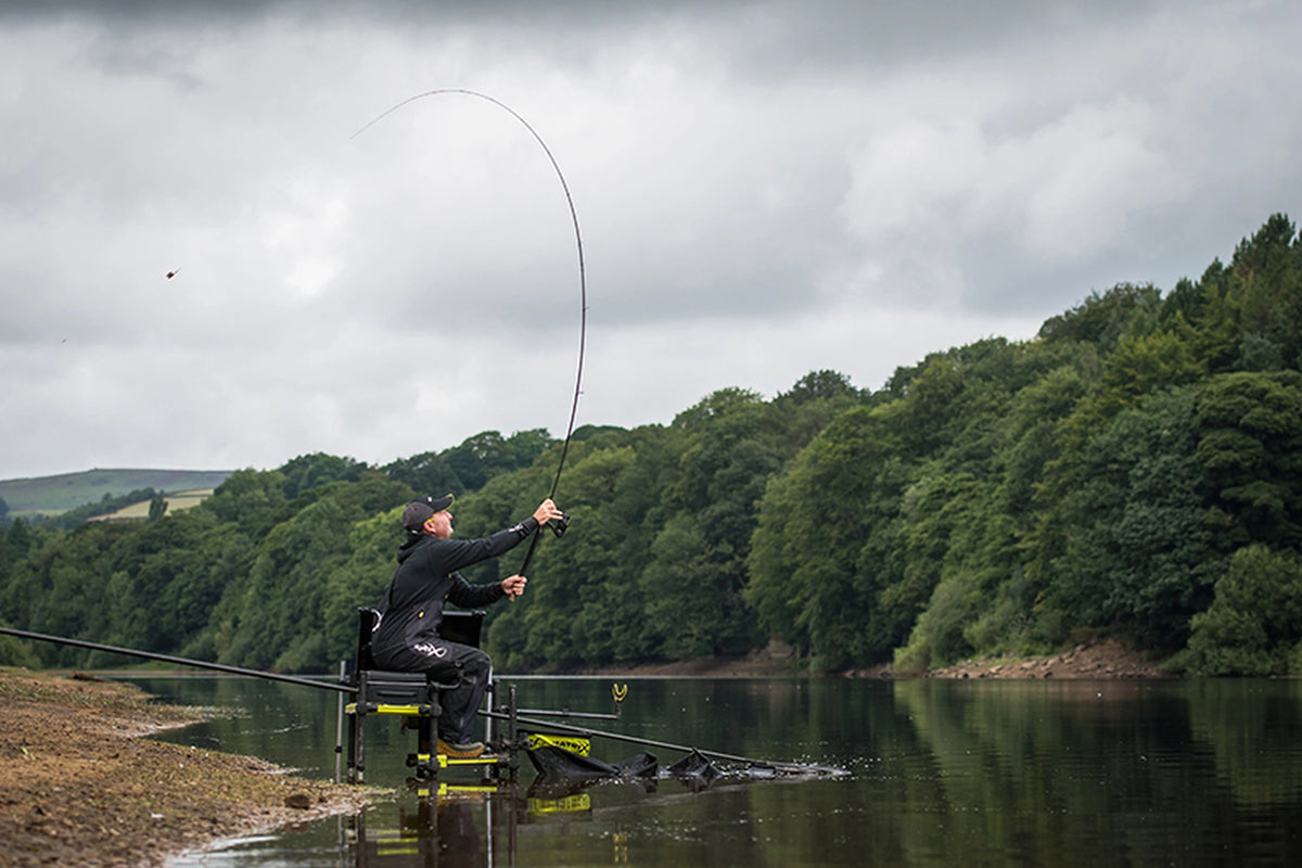 Matrix Ethos XR-S Feeder Rod in gebruik – zittende visser werpt de montage uit met een sterk gebogen hengel aan een meer