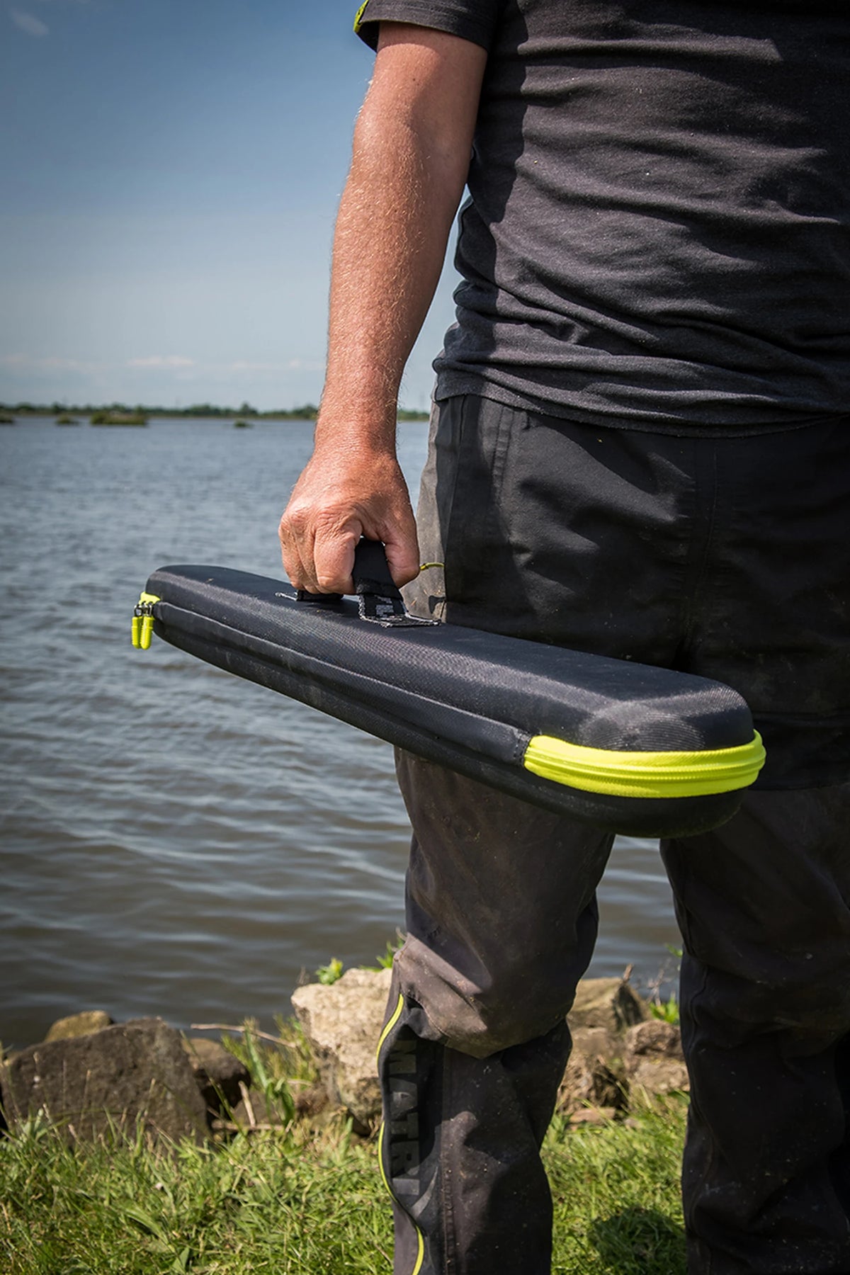 Matrix EVA Feeder Tip Case – visser draagt de gesloten etui aan de zwarte draaggreep langs de waterkant