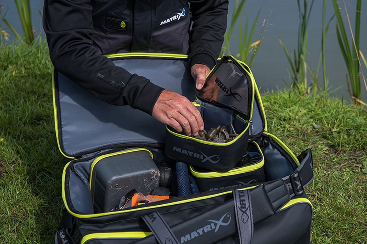 Matrix Horizon X Compact Carryall – visser met geopend opbergtasje boven de gevulde tas aan het water