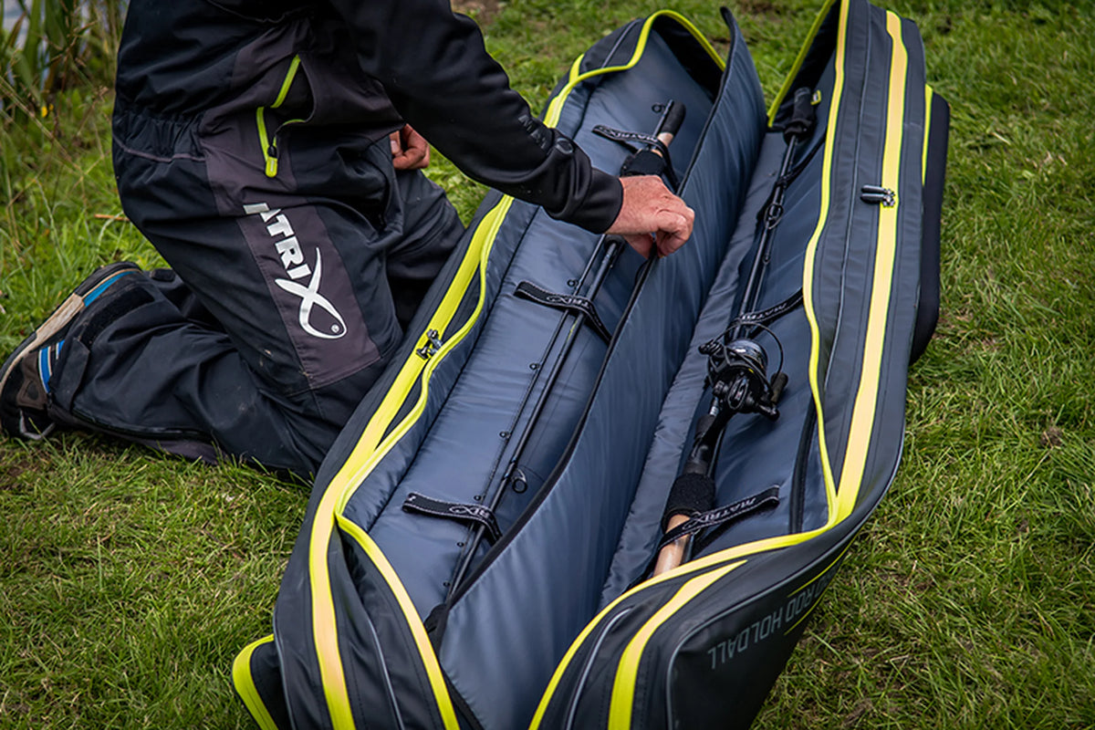 Matrix Horizon X Rigid Rod Holdall 2-4 – visser neemt een hengel uit het geopende foedraal met gevoerde vakken in het gras
