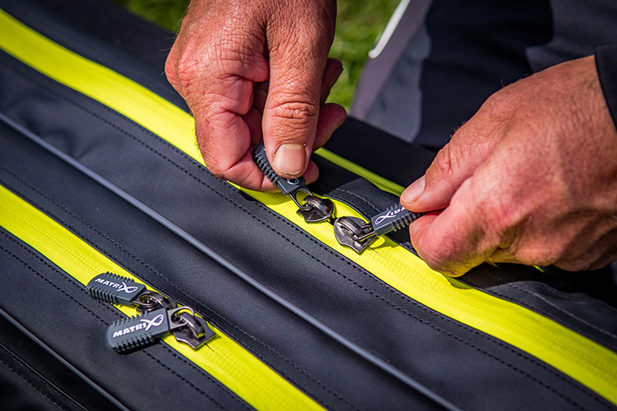 Matrix Horizon X Rigid Rod Holdall 2-4 – handen bedienen de Matrix-ritstrekkers op de gele ritsen van het foedraal
