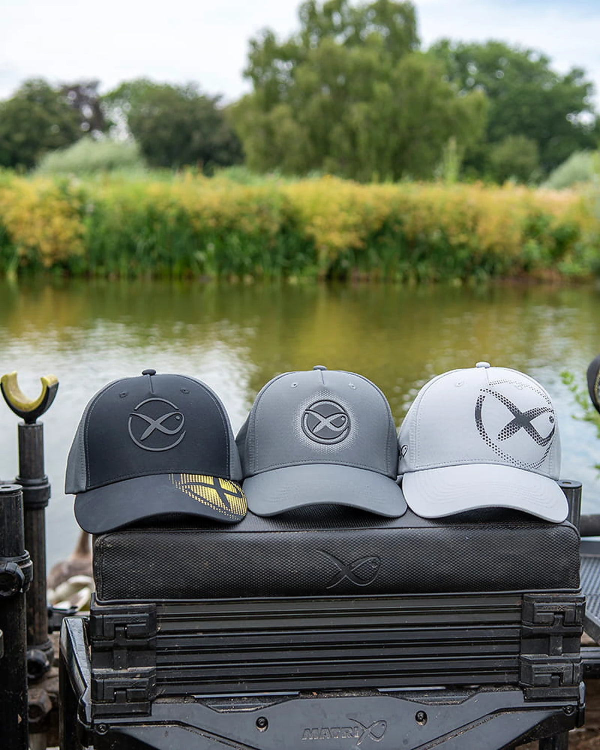 Matrix-pettenreeks aan de waterkant – Faded Print Cap Dark Grey in het midden van drie petten op een zitkist