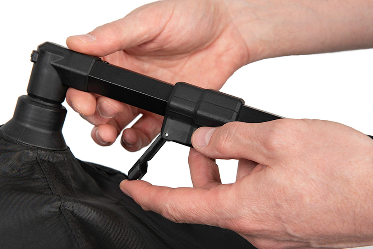 Matrix Pro Bait Brolly – handen openen de klemhendel voor de lengteverstelling van de zwarte steunarm boven de kap