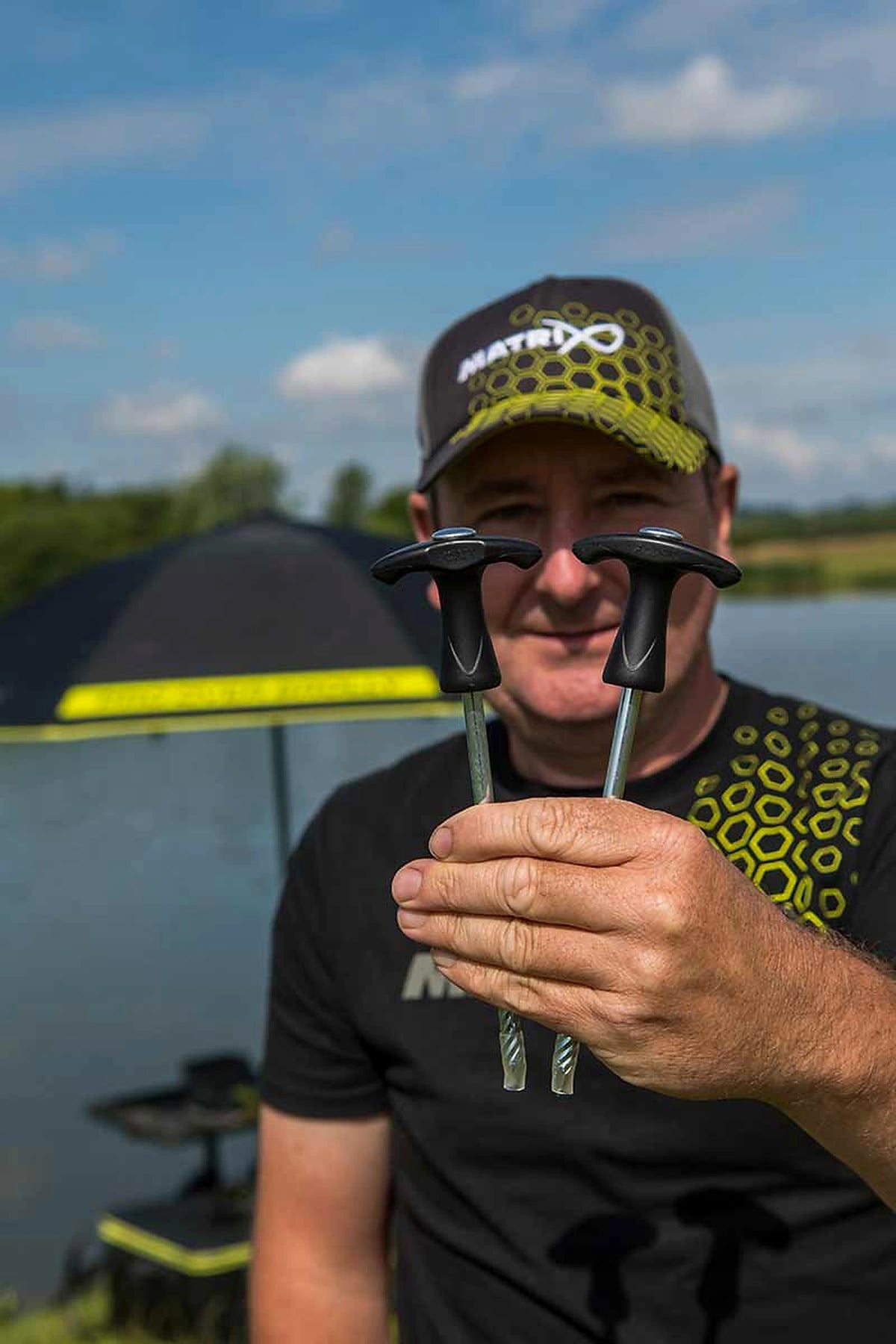 Matrix Pro Over Brolly 45 Inch – visser toont twee metalen schroefharingen met zwarte T-grepen voor de paraplu aan het water