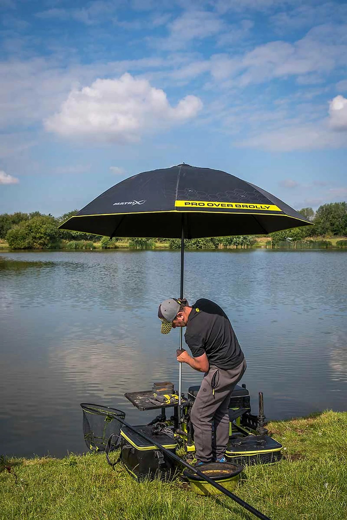 Matrix Pro Over Brolly 45 Inch – overzicht van de geopende paraplu terwijl een visser de steel bij zijn zitkist aan de waterkant afstelt
