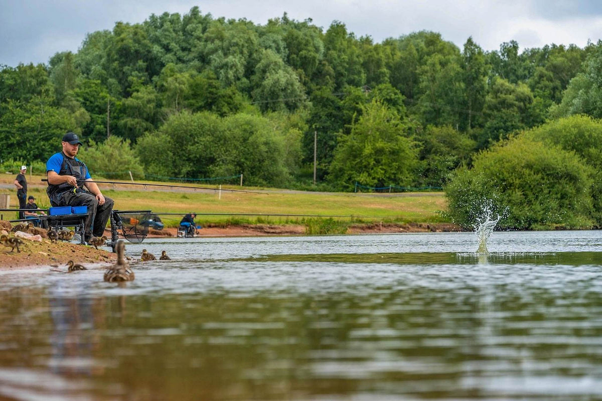 Preston Bait Up Xtreme voerhengel – visser aan de waterkant met de inslag van de voerkorf in het water