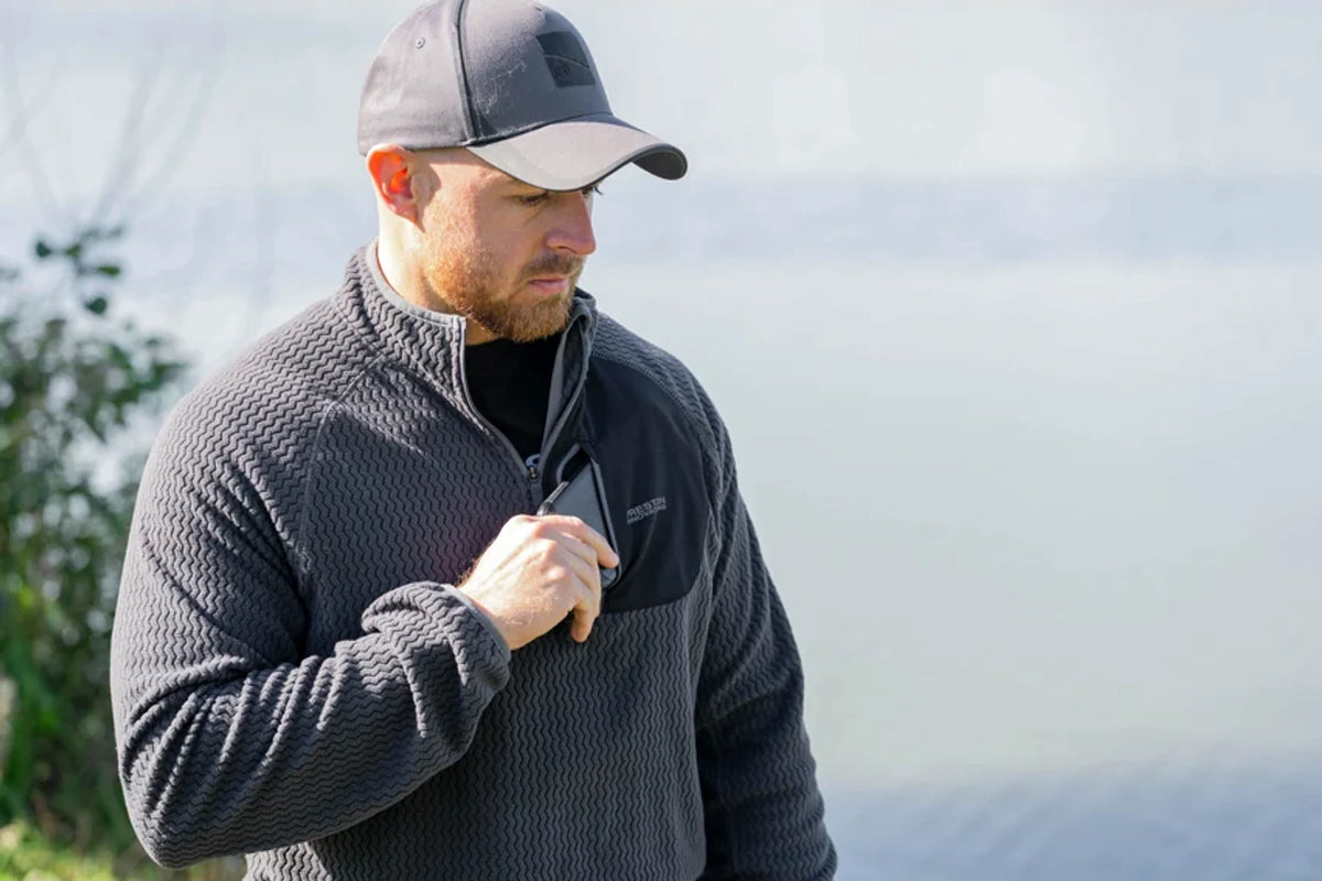 Preston Core Collection Zig Zag Fleece gedragen aan het water, met geopende kraag en zwart borstvak