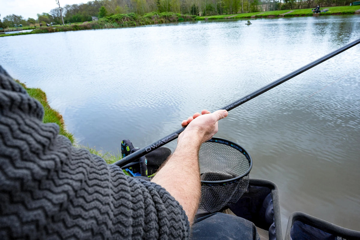 Preston DWA Kits Carp-topset in de hand van een visser aan de waterkant, met schepnet en zichtbare DWA CARP-opdruk