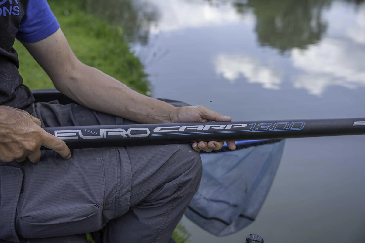 Close-up van de EURO CARP 1300-opdruk op de Preston vaste hengel in de handen van een visser