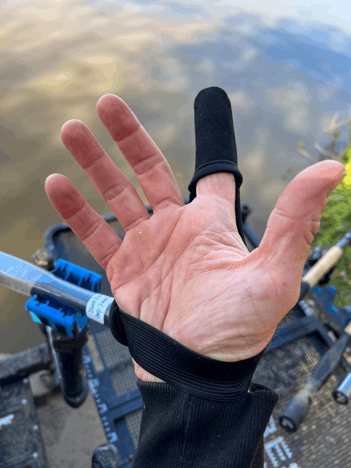 Preston Extremity Finger Stall gedragen aan de waterkant, met open handpalm, zwarte vingertop en polsband