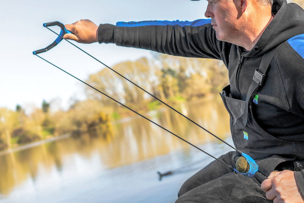 Visser spant de zwarte elastieken van de Preston Groundbait Catapult aan, met een voerbal in de pouch