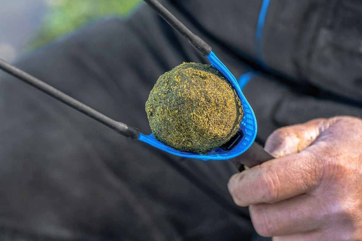 Ronde voerbal in de blauwe Preston Groundbait-pouch, met de trekband in een hand