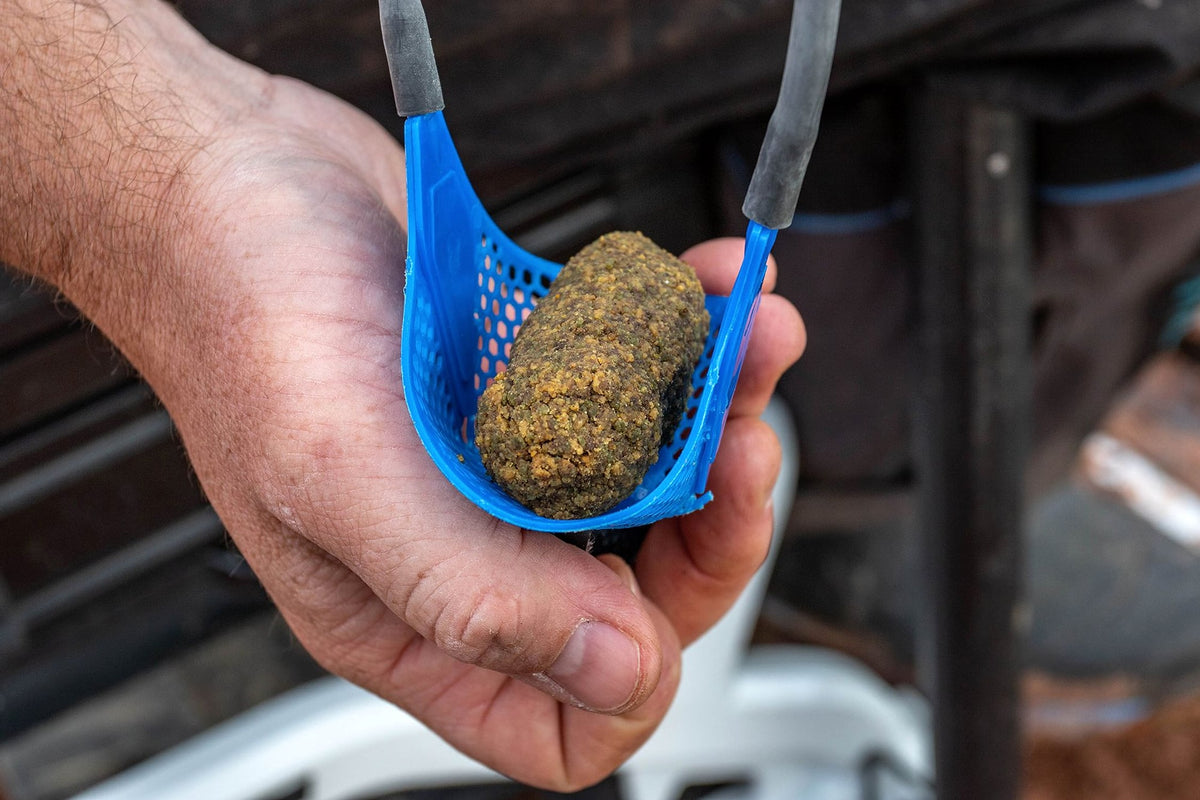 Hand ondersteunt een blauwe Preston Groundbait-pouch met een langwerpige voerbal