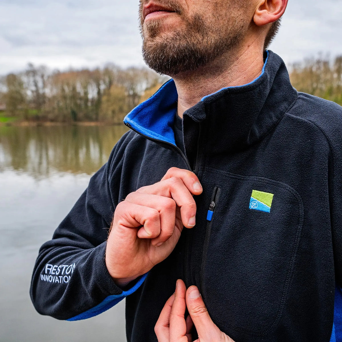 Preston Micro Fleece – detail van de bediening van de hoofdrits, blauwe kraagvoering en borstbadge