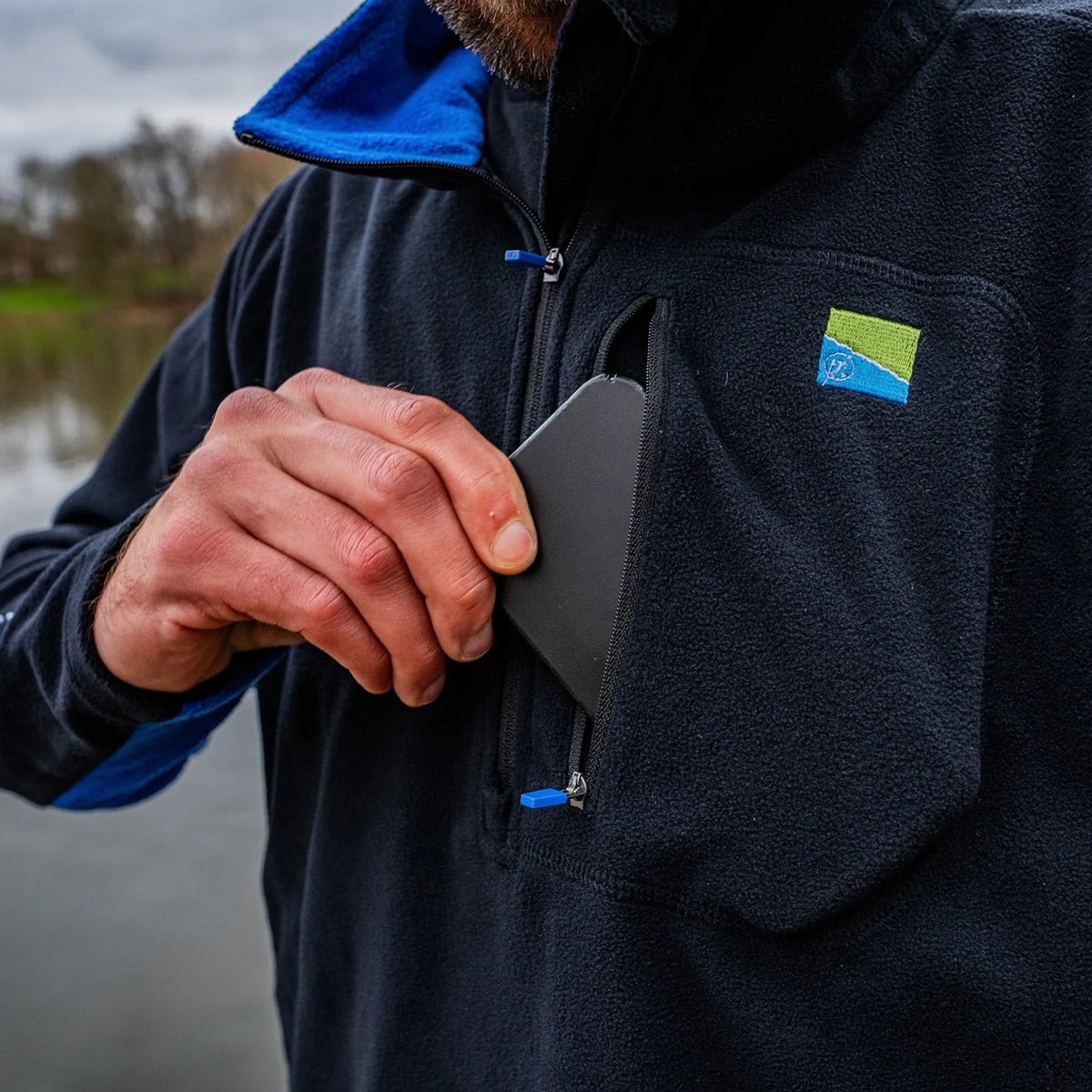 Preston Micro Fleece – detail van een telefoon in de borstzak en de blauwe ritstrekker