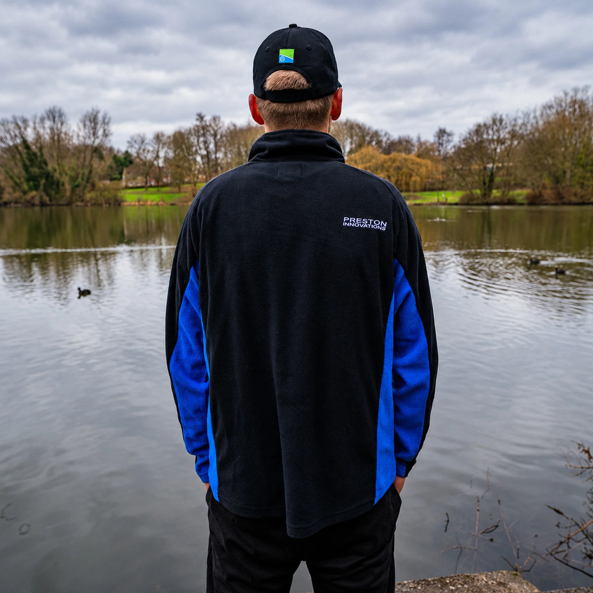 Preston Micro Fleece, achteraanzicht tijdens het dragen aan de vijver met blauwe zijpanelen en Preston-rugopdruk