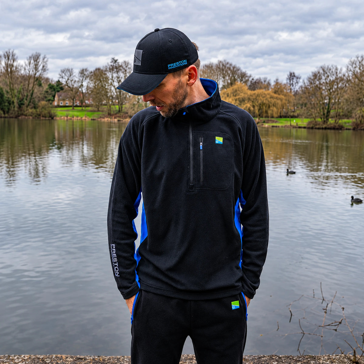 Preston Micro Fleece, gedragen aan de vijver met blauwe zijpanelen en Preston-mouwopdruk