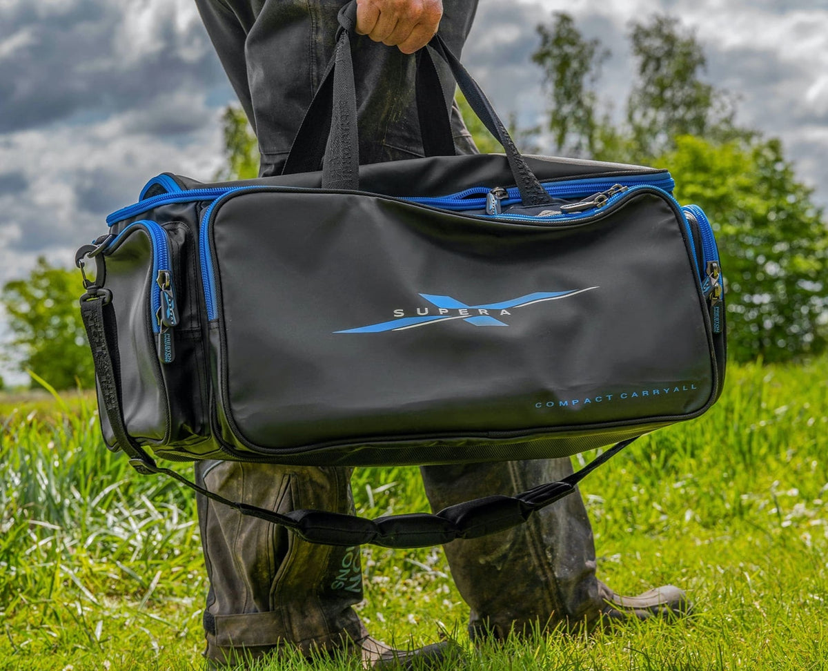 Preston Supera X Compact Carryall wordt aan de handgrepen gedragen, met de schouderriem onder de tas