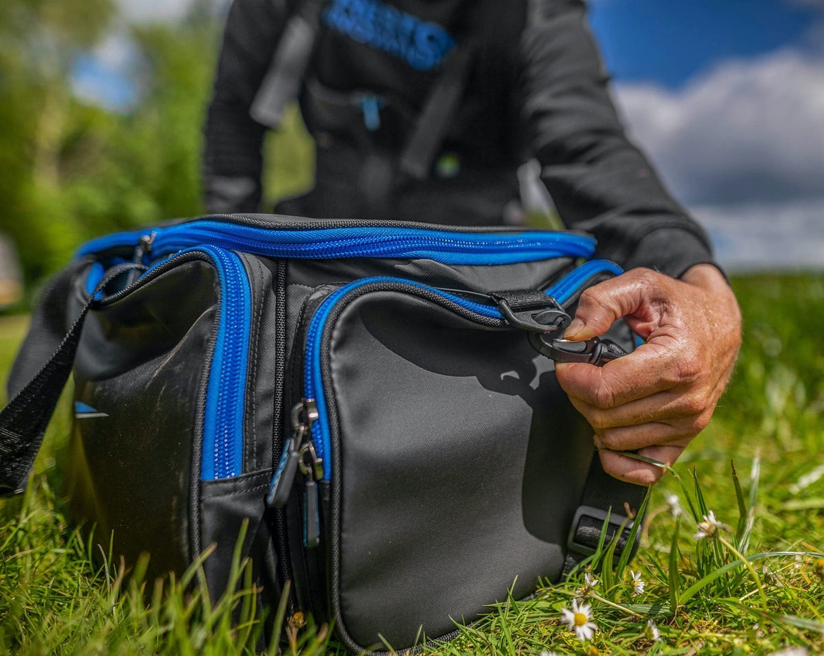 Preston Supera X Compact Carryall: een hand klikt de schouderriem los van de draagtas