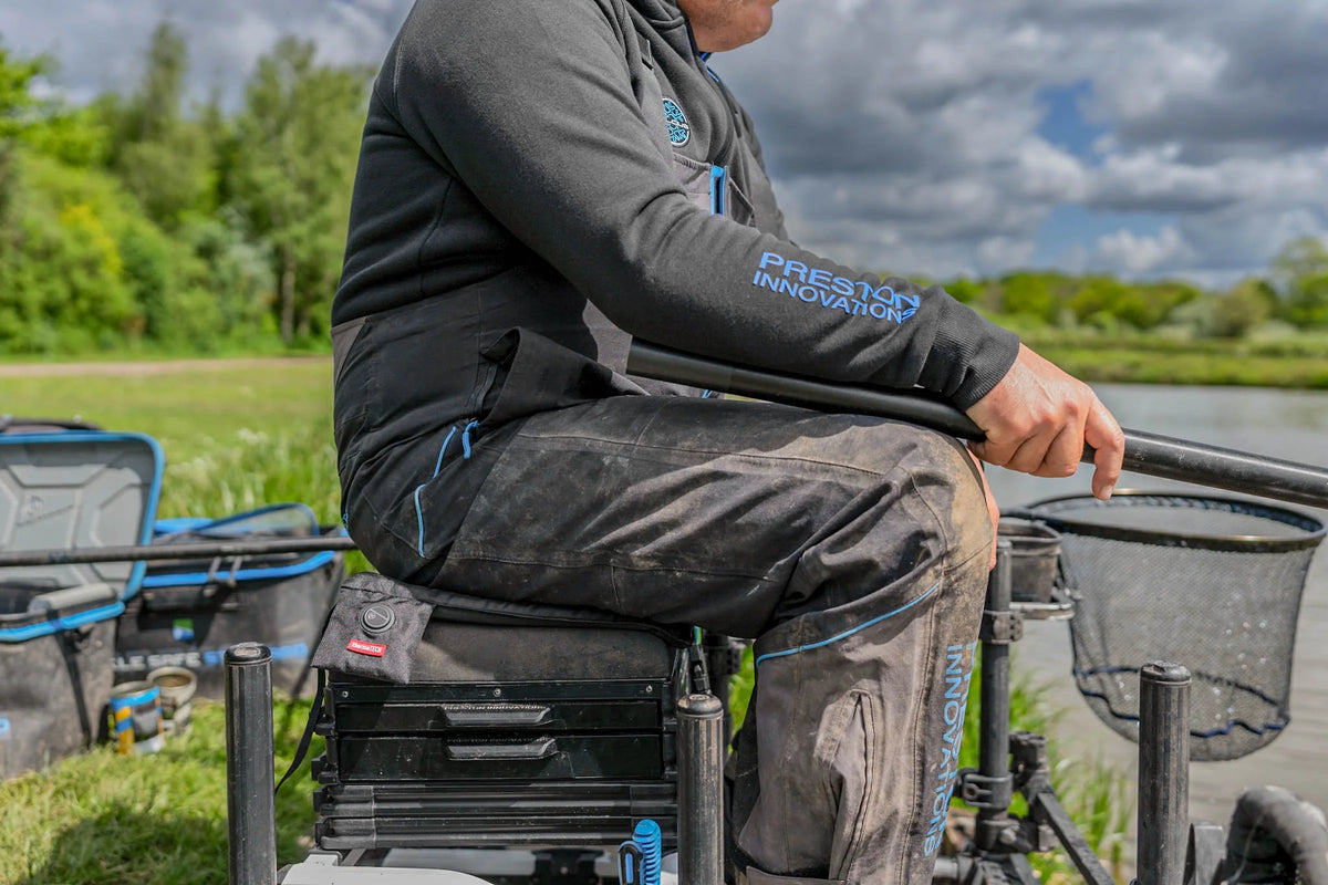 Preston ThermaTech verwarmd zitkussen in gebruik aan de waterkant – zijaanzicht met bediening naast de visser