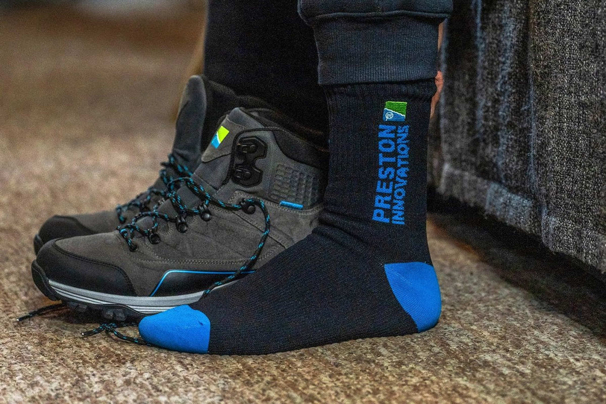 Zwart-blauwe Preston Waterproof Sock aan de voet naast een uitgetrokken visschoen, met het Preston-logo zichtbaar