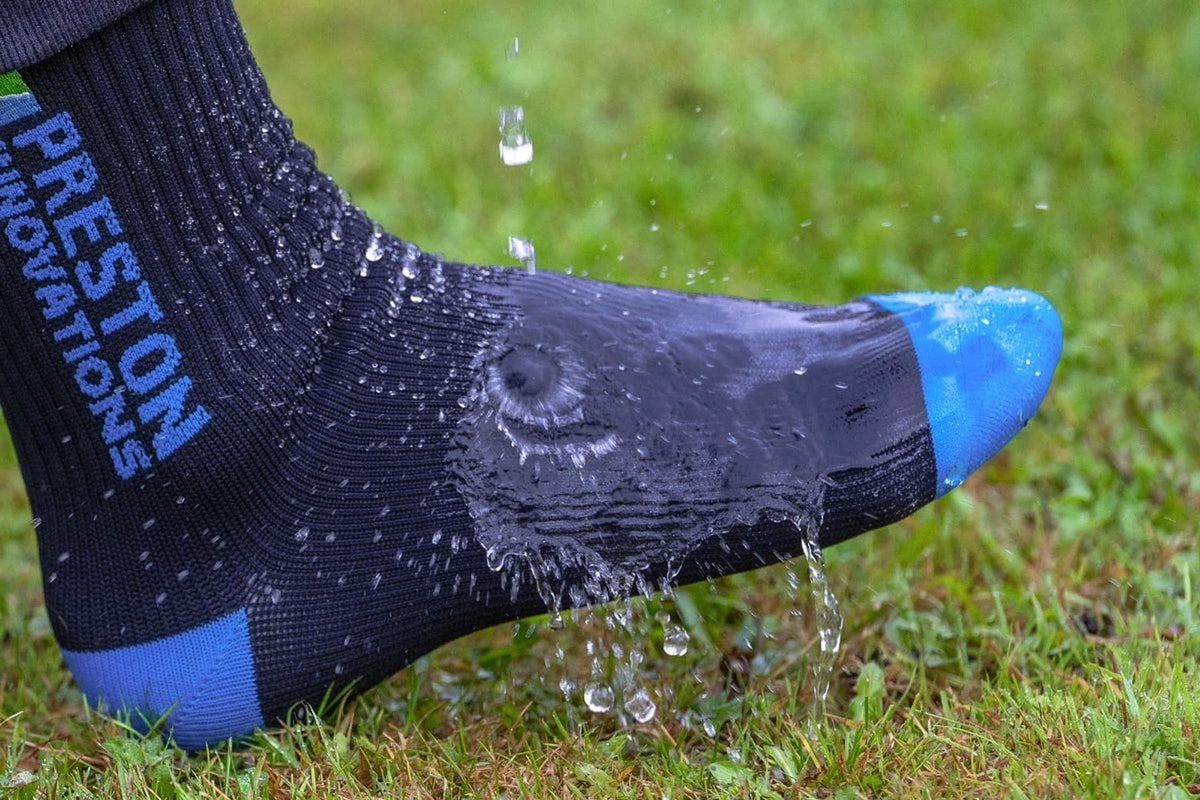 Water stroomt over een gedragen Preston Waterproof Sock met blauwe teen en hiel, op gras
