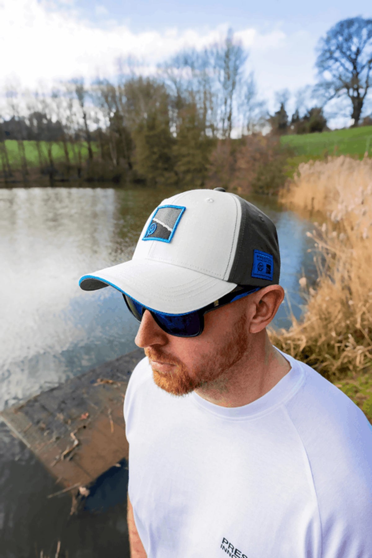 Preston White Drift Cap gedragen schuin van boven, met het water en riet op de achtergrond