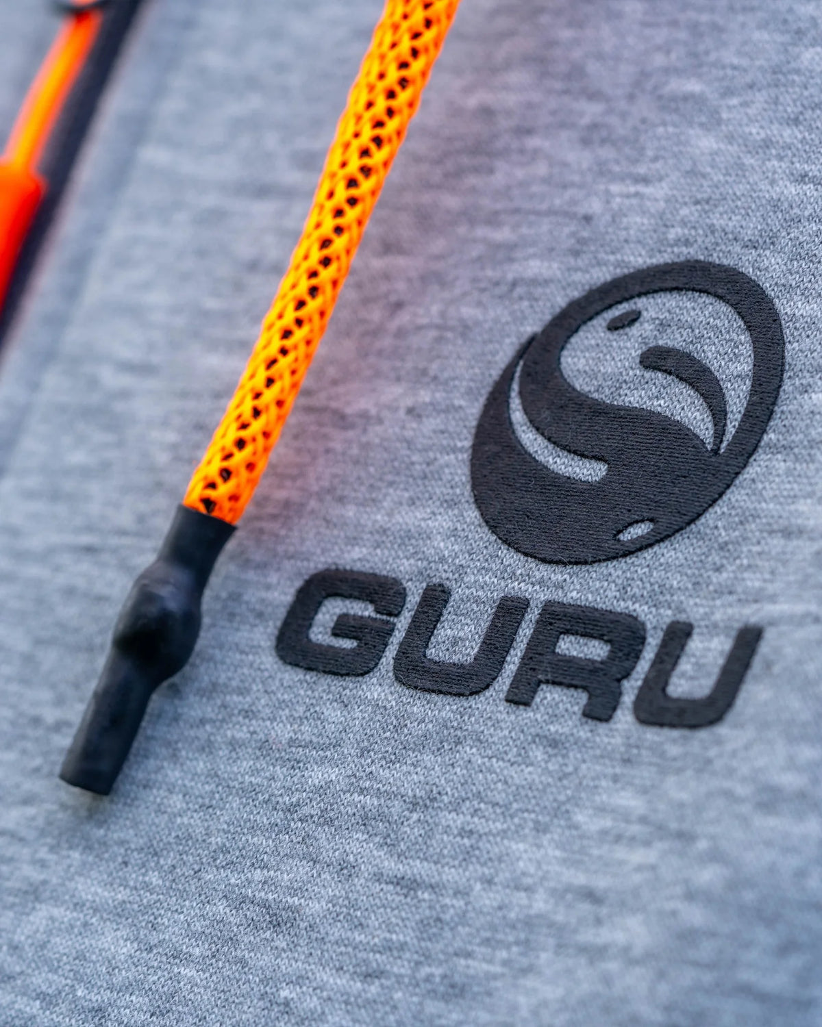 Guru Aventus Hoodie Grey, detail van geborduurd Guru-borstlogo en oranje capuchonkoord