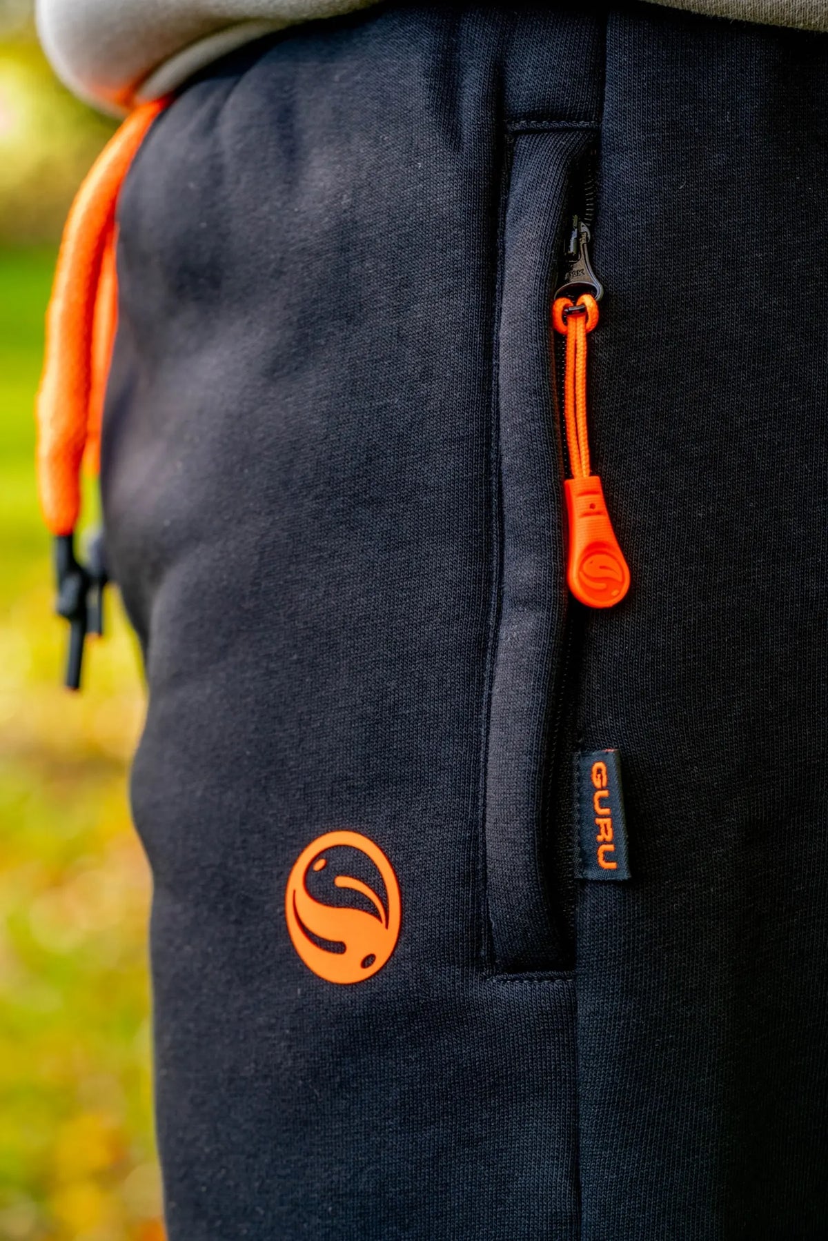 Guru Black Joggers – detail van ritssluiting en oranje Guru-embleem