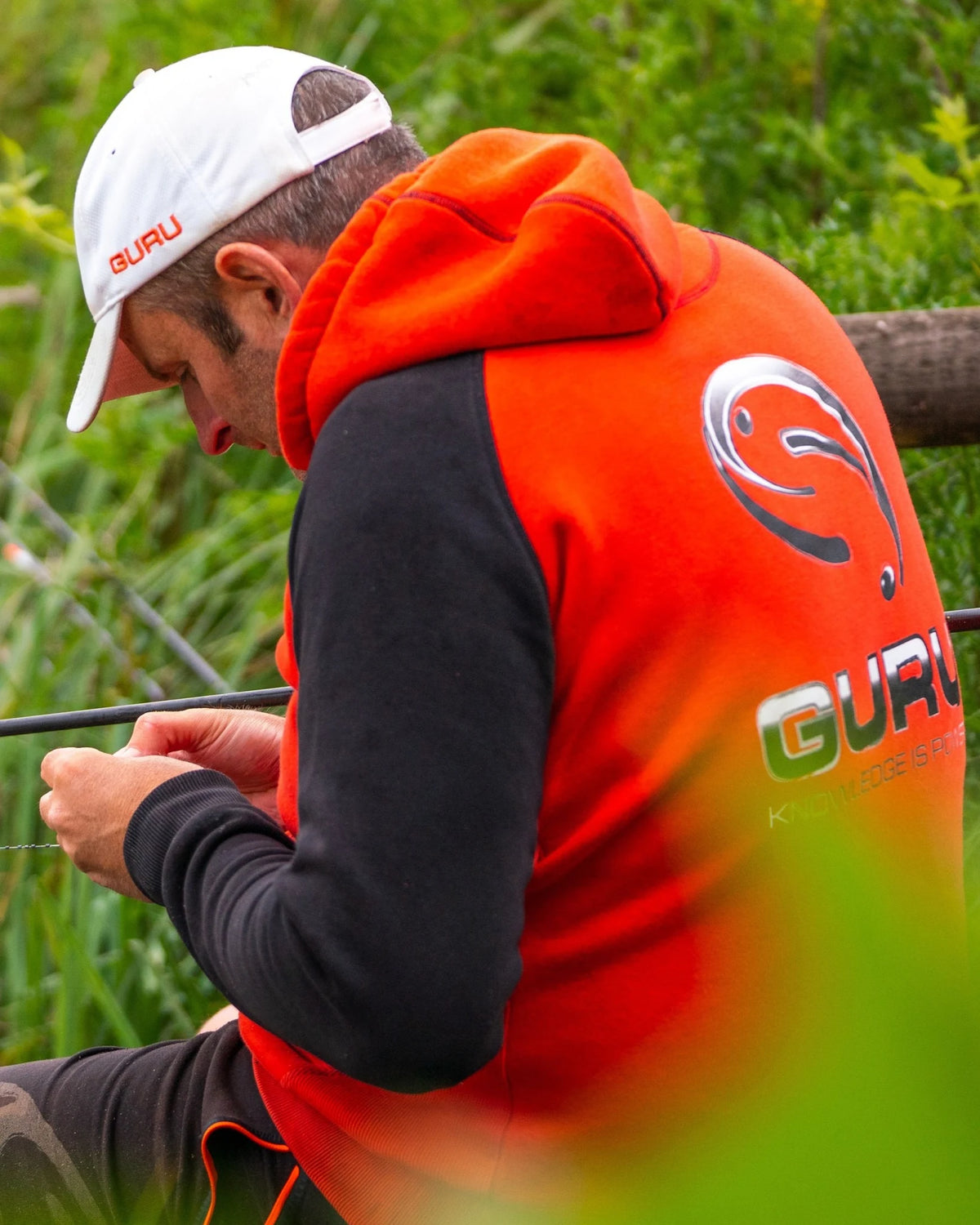 Guru Hoodie Red/Black, gedragen rugaanzicht met groot Guru-logo tijdens het vissen